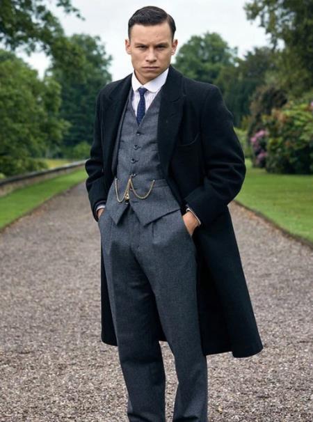a man wearing a gray vest and pants and black overcoat, complete with accessories but no hat just like how Michael Gray of Peaky Blinders wears his suit