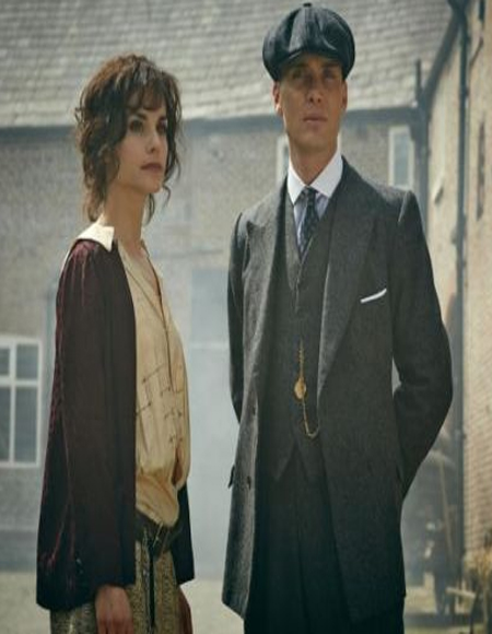 Thomas Shelby wearing a grey single-breasted Peaky Blinders suit and standing beside a woman